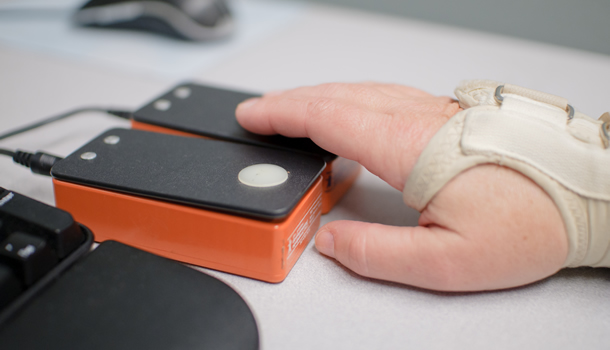 A hand, wearing a brace, presses a switch to operate a computer.
