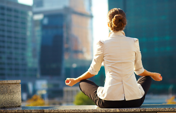 Woman in business clothes meditating, city buildings in the background.