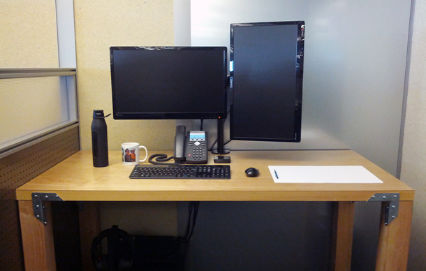A bare desk with a computer, phone, mug, thermos, and paper