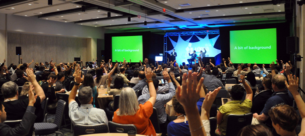 Audience members holding up their hands as they watch a presentation.